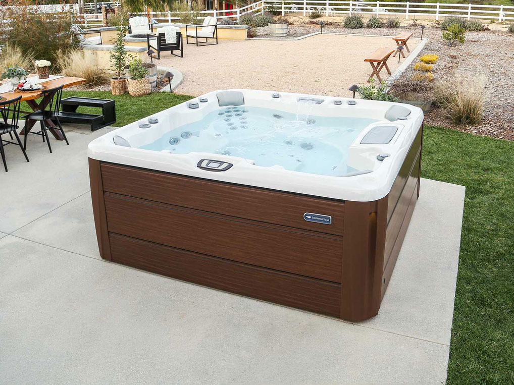 Modern hot tub with brown, wood-like exterior and clear blue water. On top of a patio in a backyard near and outdoor seating area. Multi-person hot tub perfect for homeowners in New Fairfield, CT.