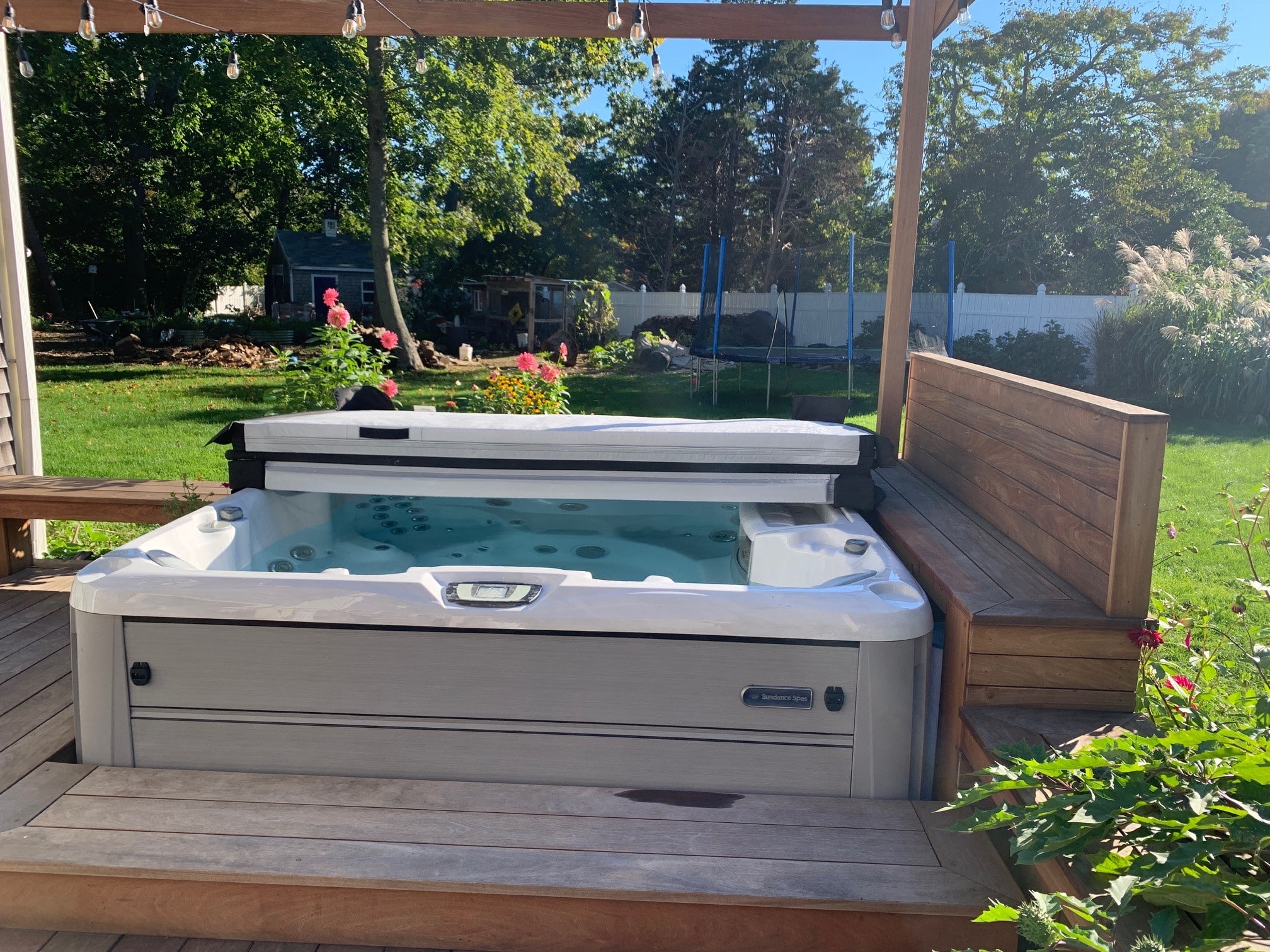 Backyard of a family home in Yorktown Heights, NY. Shows family hot tub, hot tub seating, and other recreational activites in the back including a trampoline, garden, shed, and chicken coop.
