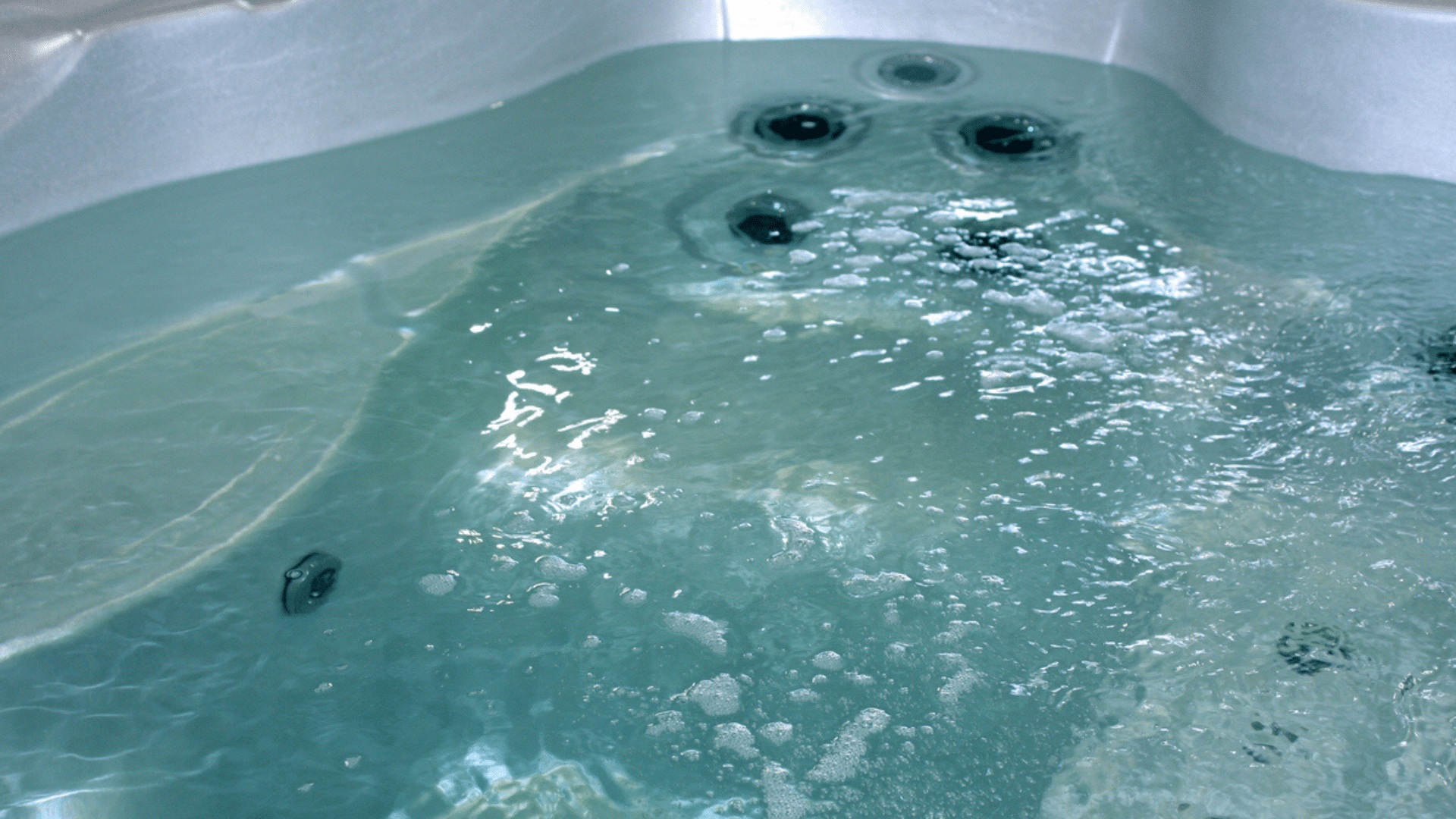 Hot tub on deck under blue sky near white vinyl fence. Cover is off after easy removal, showcasing hot tub cover options at Nejame & Sons in Danbury, CT & Carmel, NY.