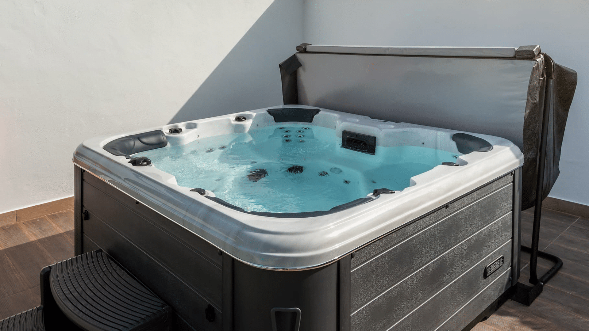 Hot tub on deck under blue sky near white vinyl fence. Cover is off after easy removal, showcasing hot tub cover options at Nejame & Sons in Danbury, CT & Carmel, NY.