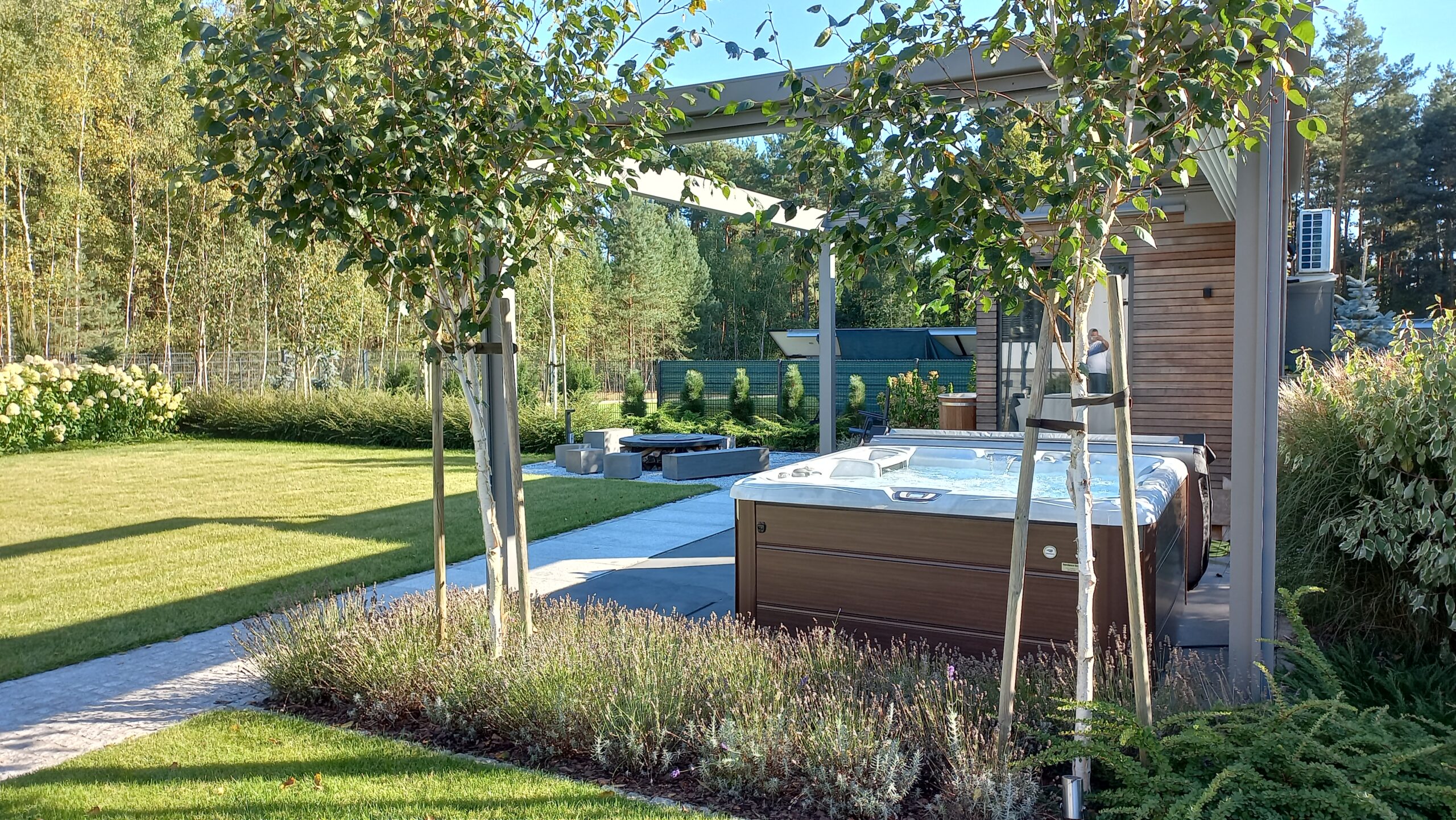 Mahopac home's backyard featuring Sundance hot tub, seating area in background, privacy headges, and small decorative trees.