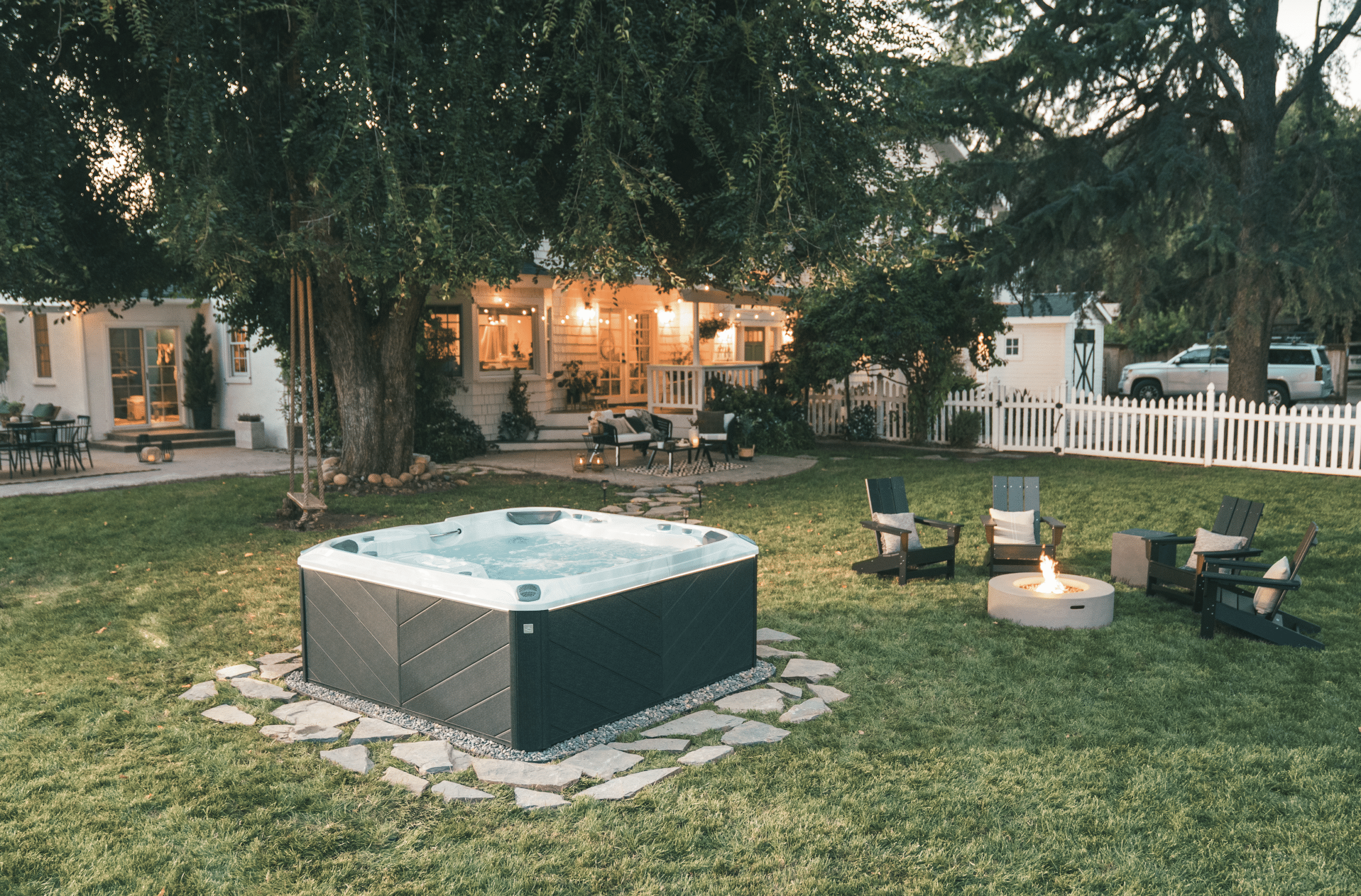 Mahopac home's backyard featuring Sundance hot tub, seating area in background, privacy headges, and small decorative trees.