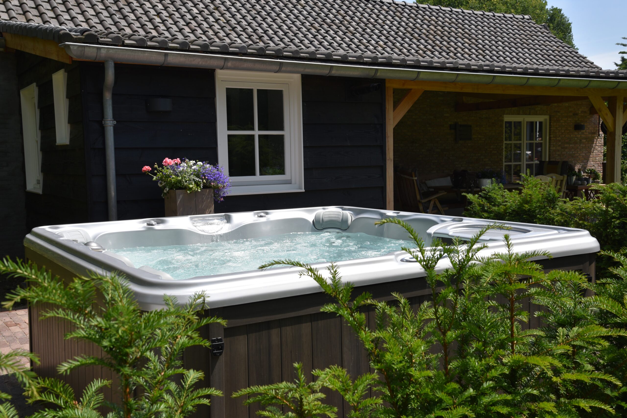 Mahopac home's backyard featuring Sundance hot tub, seating area in background, privacy headges, and small decorative trees.