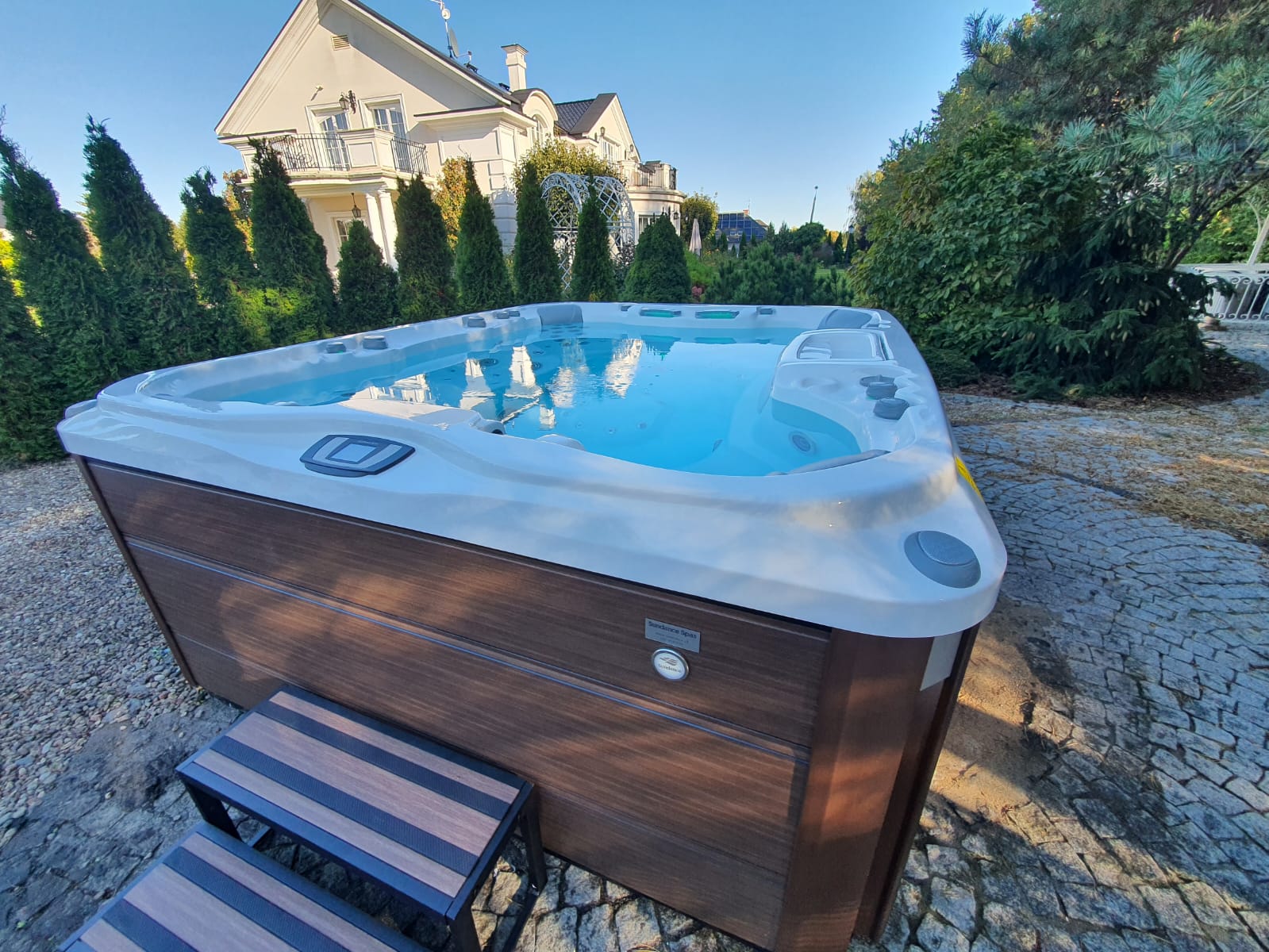 Hot tub at Somers, NY home with custom non-slip steps for mobility. Tall shrubs in background, stone patio underneath.